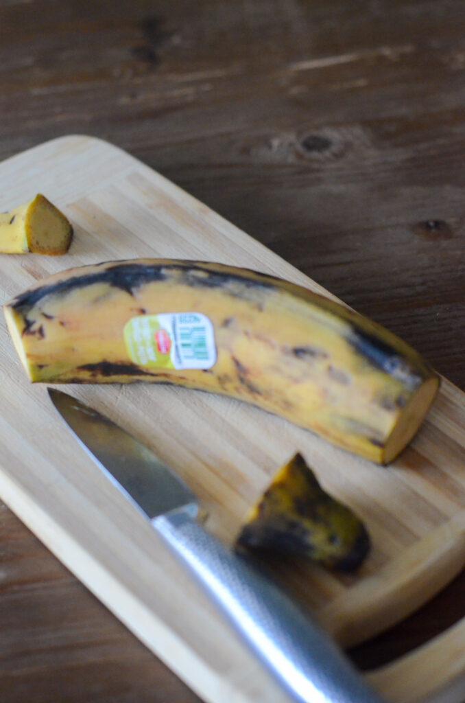 ripe yellow plantain with ends cut on cutting board with knife