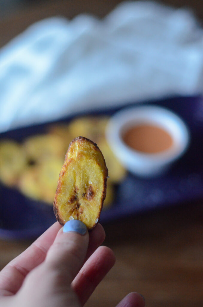 woman holds slice of air fryer plantains with sriracha mayonnaise sauce