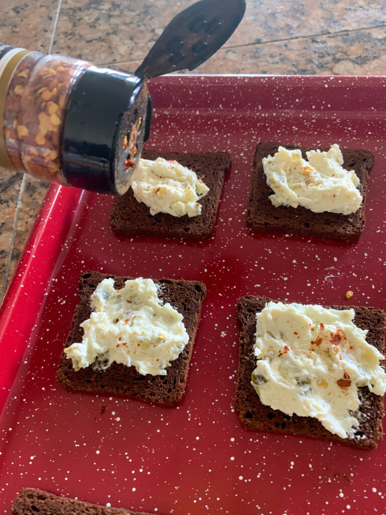 sprinkling red pepper flakes on red tray of party rye bread recipe