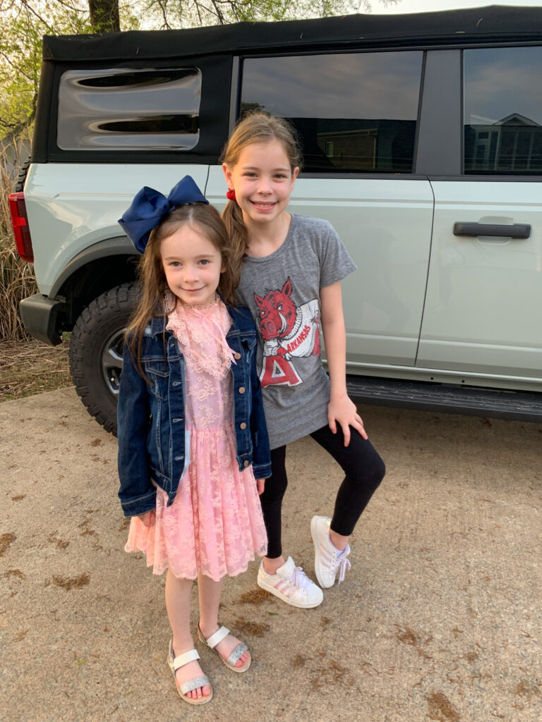 Girls dressed in vintage Easter dress and Vintage Razorback shirt for Vintage Day theme day n front of a cactus gray Ford Bronco