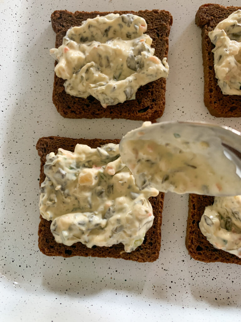  rye bread appetizer with spinach dip on spoon pouring dip