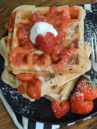 strawberry waffles stacked on black plate with strawberry hearts