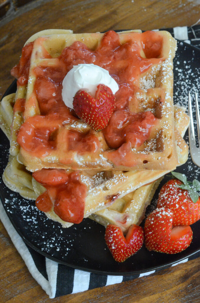strawberry waffles stacked on black plate with strawberry shaped hearts 