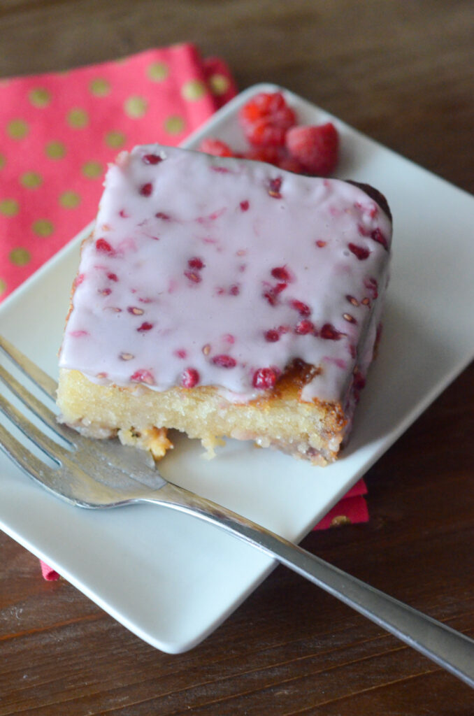 white chocolate and raspberry cake with raspberry cake glaze on white rectangular plate with polka dot napkin