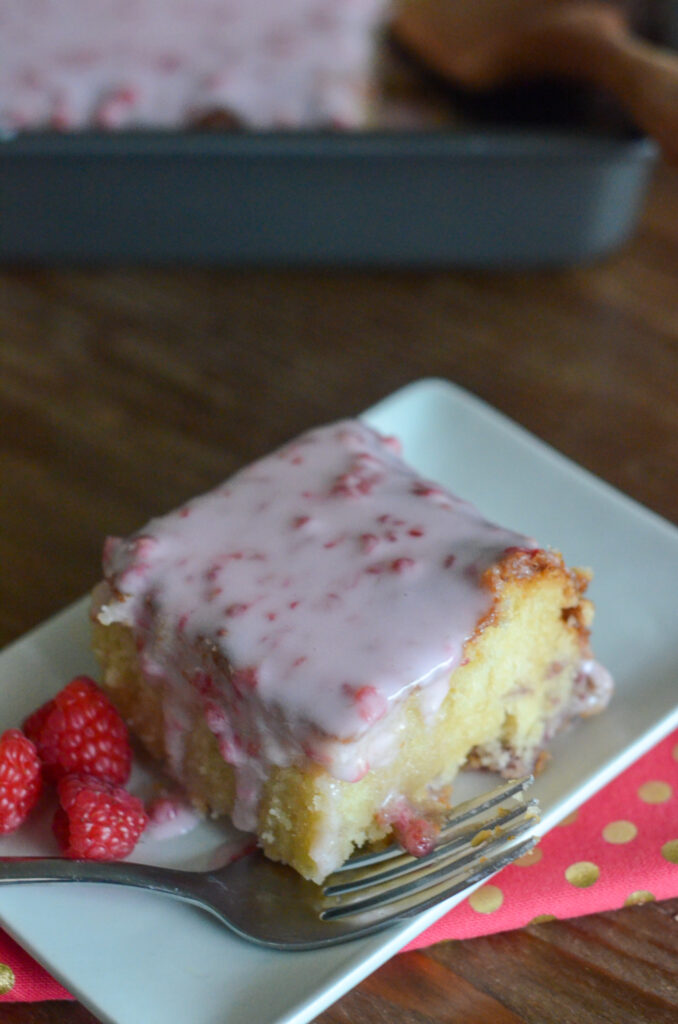 white chocolate and raspberry cake with raspberry cake glaze with fork on white plate over pink polka dot napkin