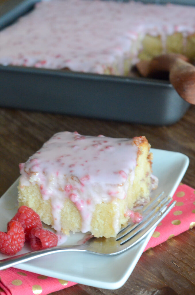 slice of white chocolate raspberry cake with icing in the batter and raspberries on the plate