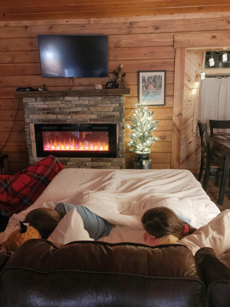children sleep on a pullout bed in front of an electric fireplace at Starlight Haven luxury Hot Springs treehouse cabins in Arkansas