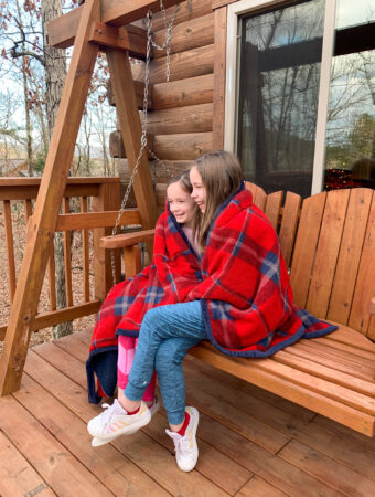 two girls swing on the deck swing at their luxury Hot Springs treehouse cabin