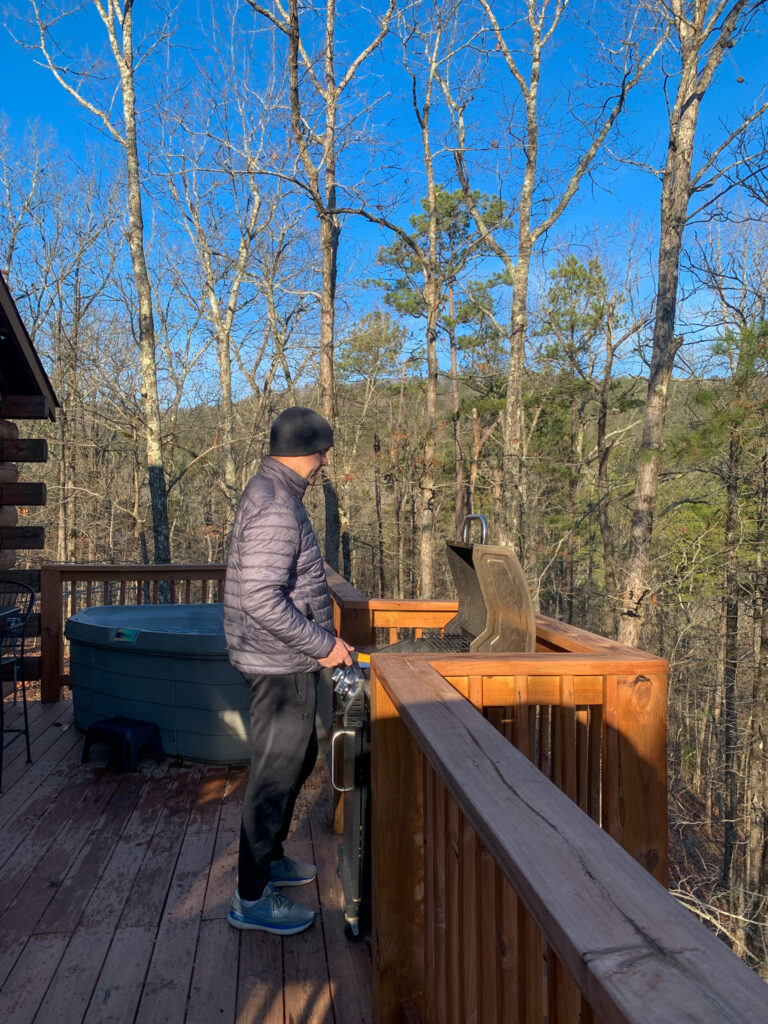 man grills on the back deck of a luxury Hot Springs treehouse cabin in January