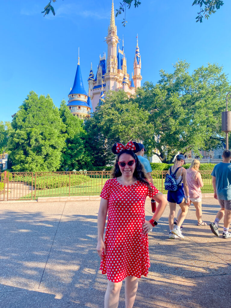 woman wears a polka dot Magic Kingdom outfit while standing in front of the castle at Magic Kingdom