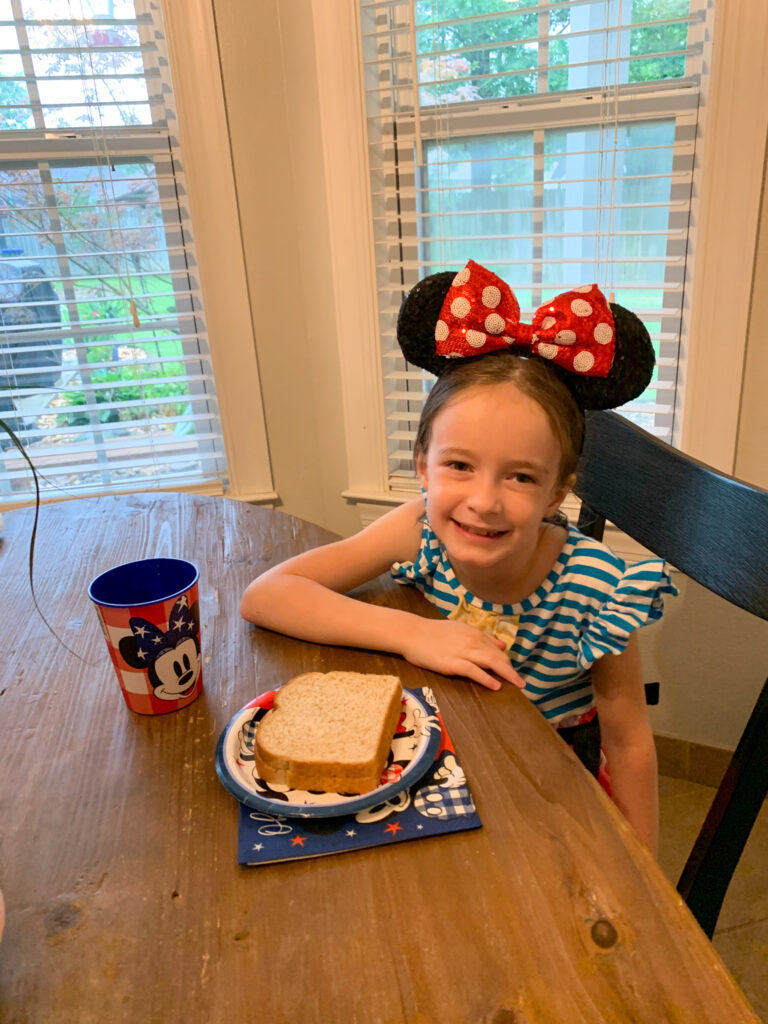 little girl smiles during her surprise Disney World trip reveal with sandwich in front of her