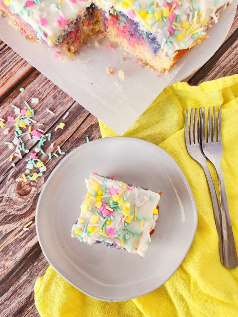 rainbow swirl cake with homemade vanilla buttercream frosting and sprinkles beside yellow napkin