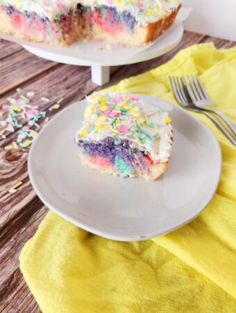 rainbow swirl cake with food coloring piece on white plate with rainbow cake in back