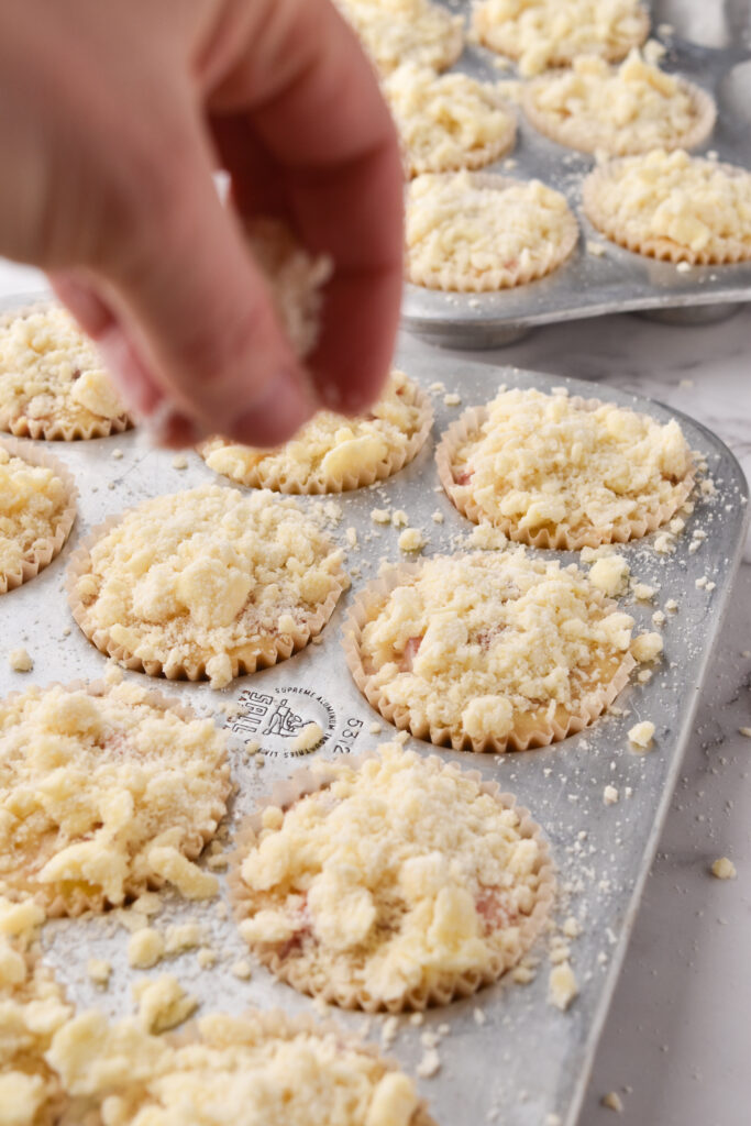 woman sprinkles streusel on strawberry crumble muffins tray