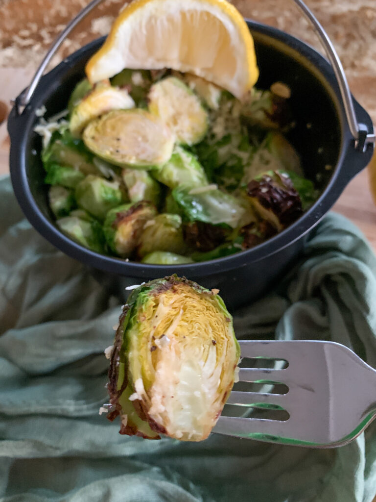 air fried Brussels sprouts on fork with the rest in air fryer skillet at back