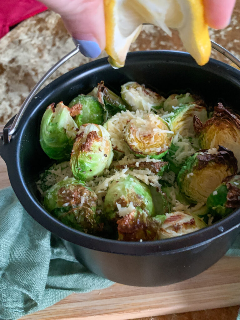 air fryer Brussels sprouts in air fryer skillet while lady squeezes lemon over