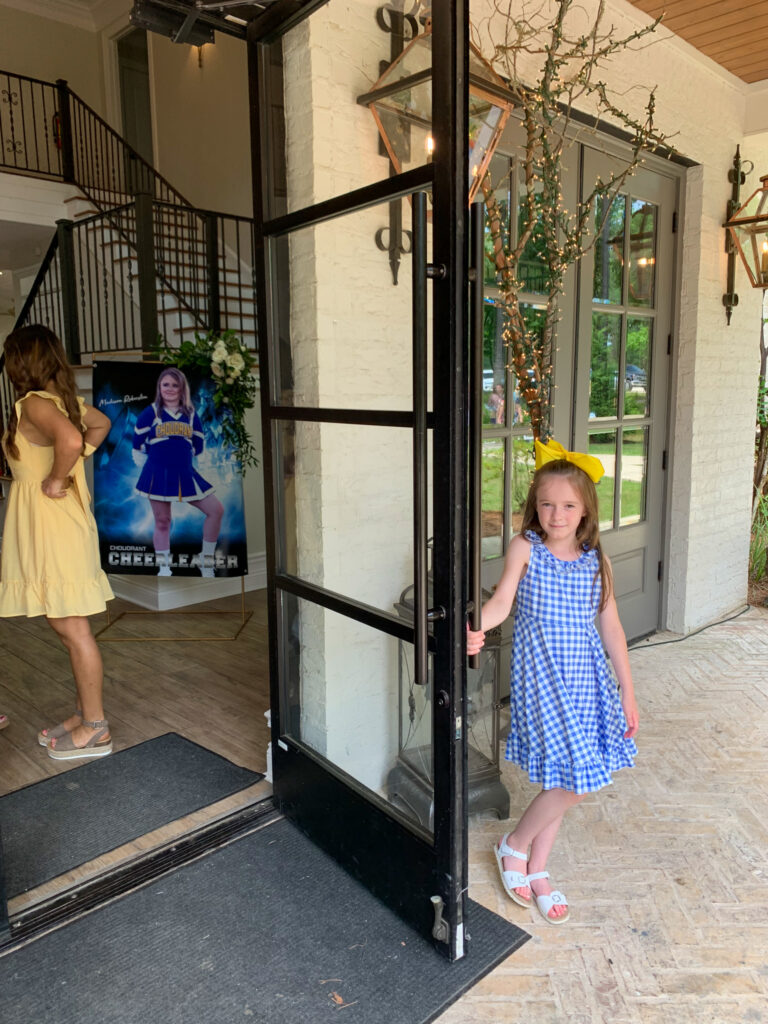 little girl holds door open for guests at high school graduation tea party at 