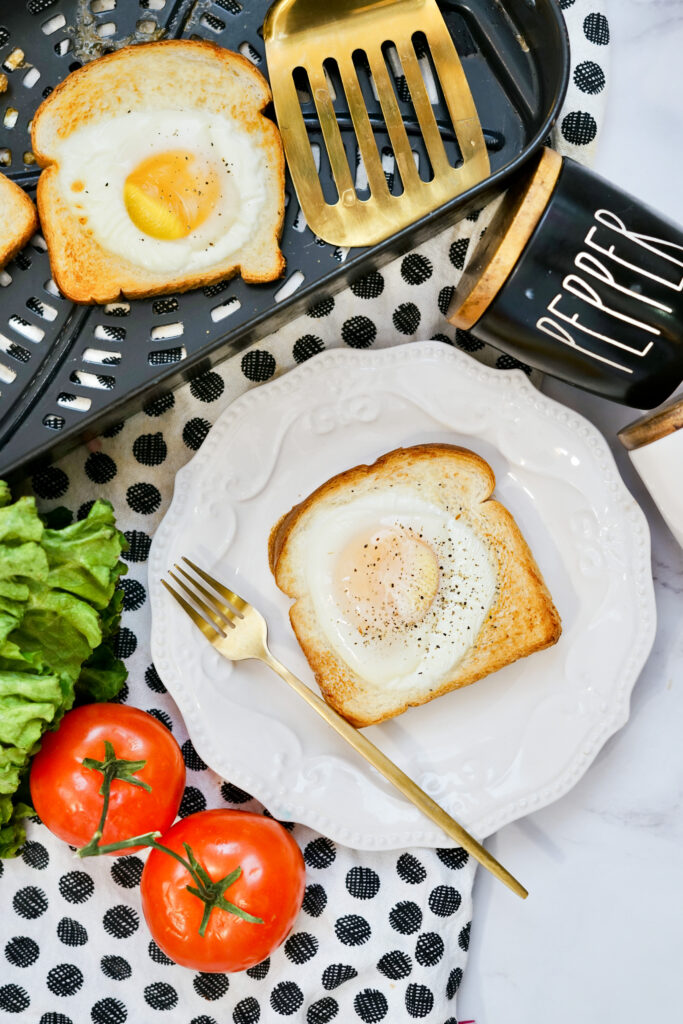 cooked air fryer egg toast on a white plate over polka dot napkin and tomatoes and tray to the side