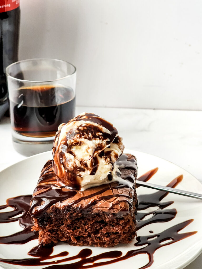 chocolate coca cola cake on a white plate with glass of Coca Cola in back
