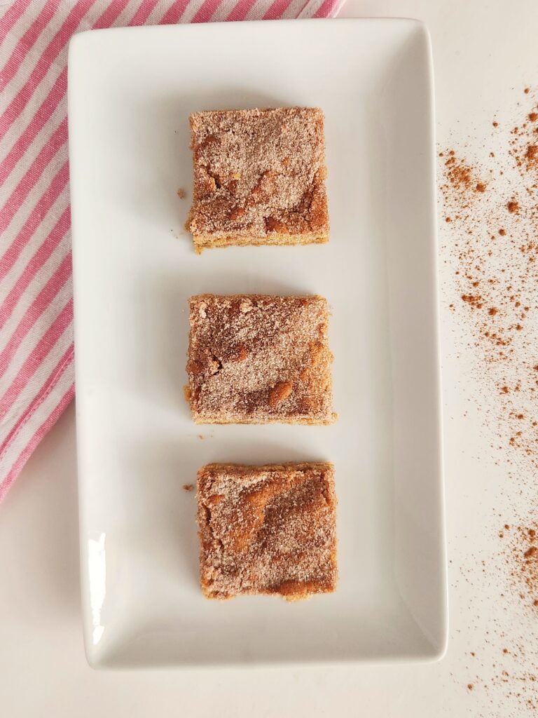 three cinnamon churro bars in a line on a white platter with striped napkin to left
