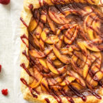 raspberry peach melba tart on white background with raspberries scattered about