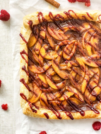 raspberry peach melba tart on white background with raspberries scattered about