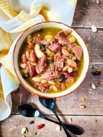 15 bean soup with ham hock in a red bowl with napkin beside in overlay image