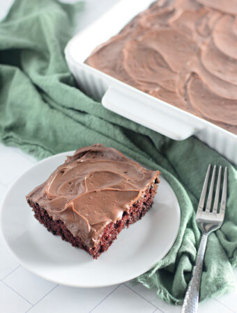 dairy free chocolate cake (chocolate crazy cake) slice on a small white plate with fork and whole cake in back