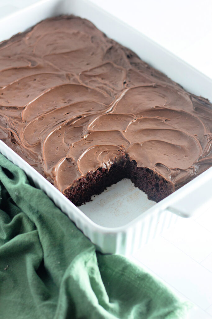 dairy free chocolate cake in white baking pan with slice removed next to a green cloth