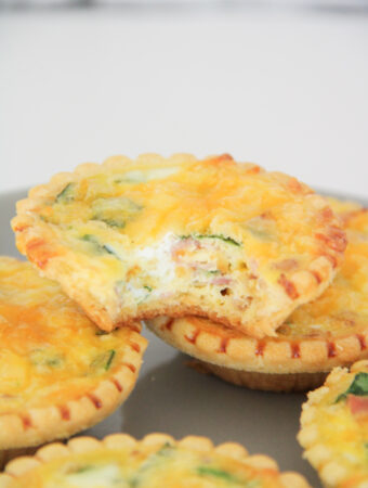 stack of mini ham and spinach quiche with bacon tarts on gray plate