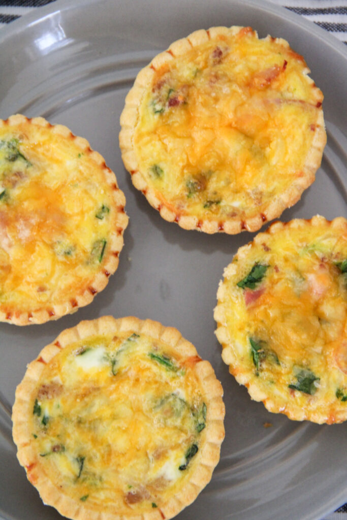 four ham and spinach quiche tarts on a gray plate