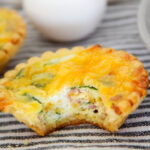 ham spinach quiche with bite taken out with eggs in back