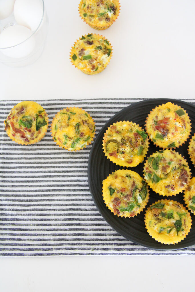 low carb crustless quiche muffins scattered over plate and striped napkin with eggs in back