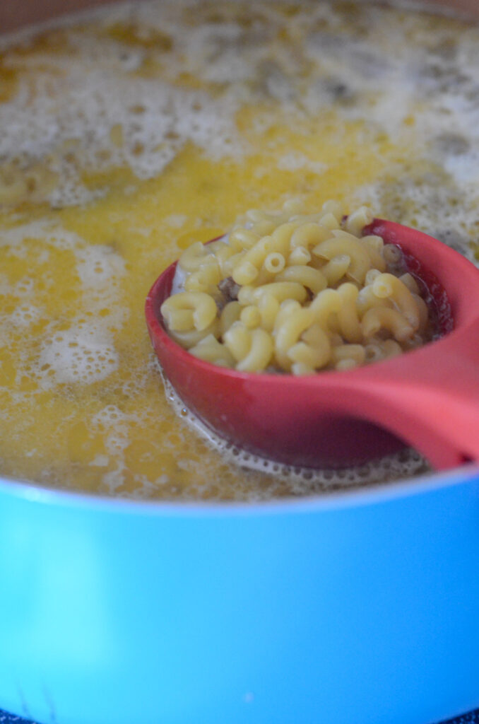 red spoonful of macaroni over pot of boiling broth