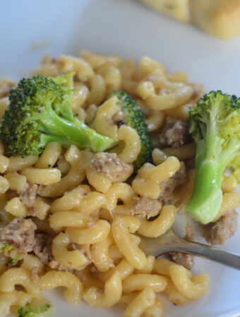 sausage broccoli macaroni on white saucer with a bread in the back