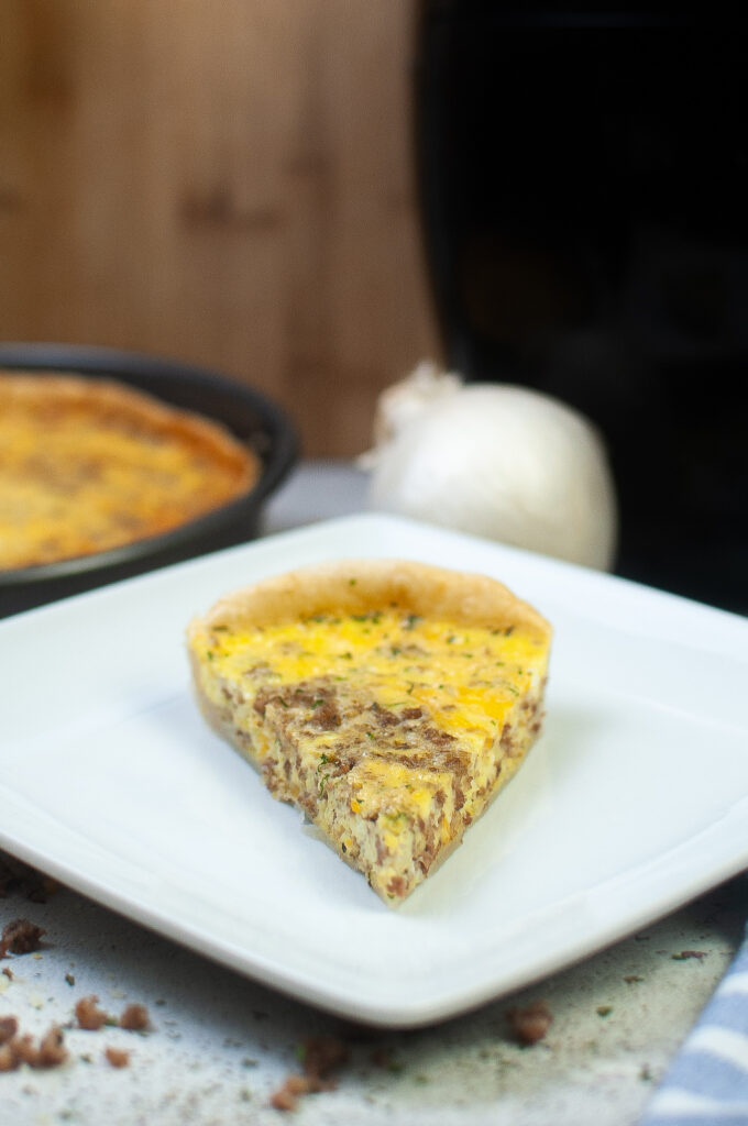 air fryer quiche with crust on white plate with onion in back