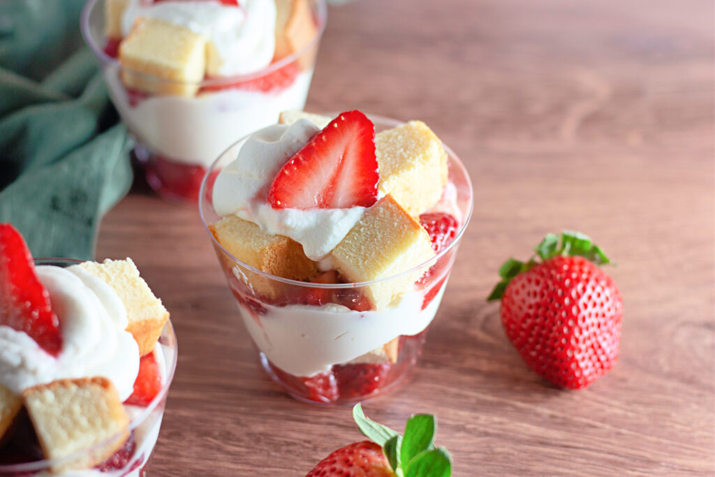 3 strawberry shortcake cups with green cloth in back and berries on table