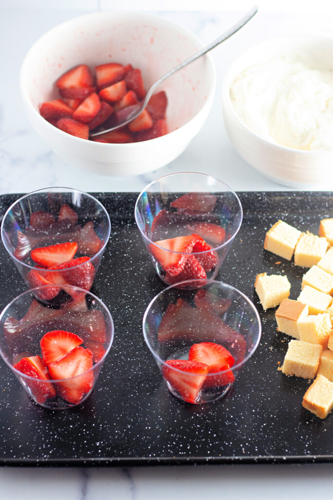 strawberries in plastic bowls on tray with more strawberries and cake cubes to side