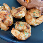 cajun butter shrimp on black plate by potato