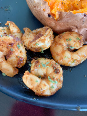 cajun butter shrimp on black plate by potato