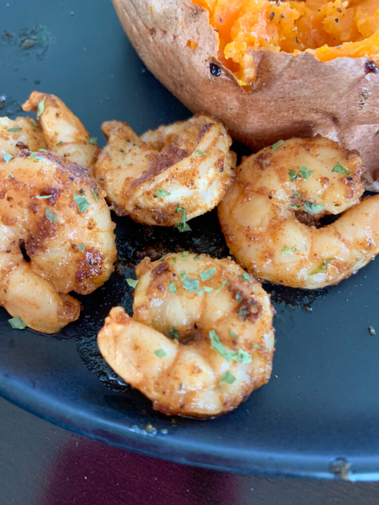 cajun butter shrimp on black plate by potato