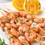 lemon garlic shrimp skewers on white platter with lemons in back