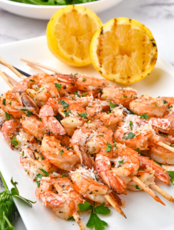 lemon garlic shrimp skewers on white platter with lemons in back