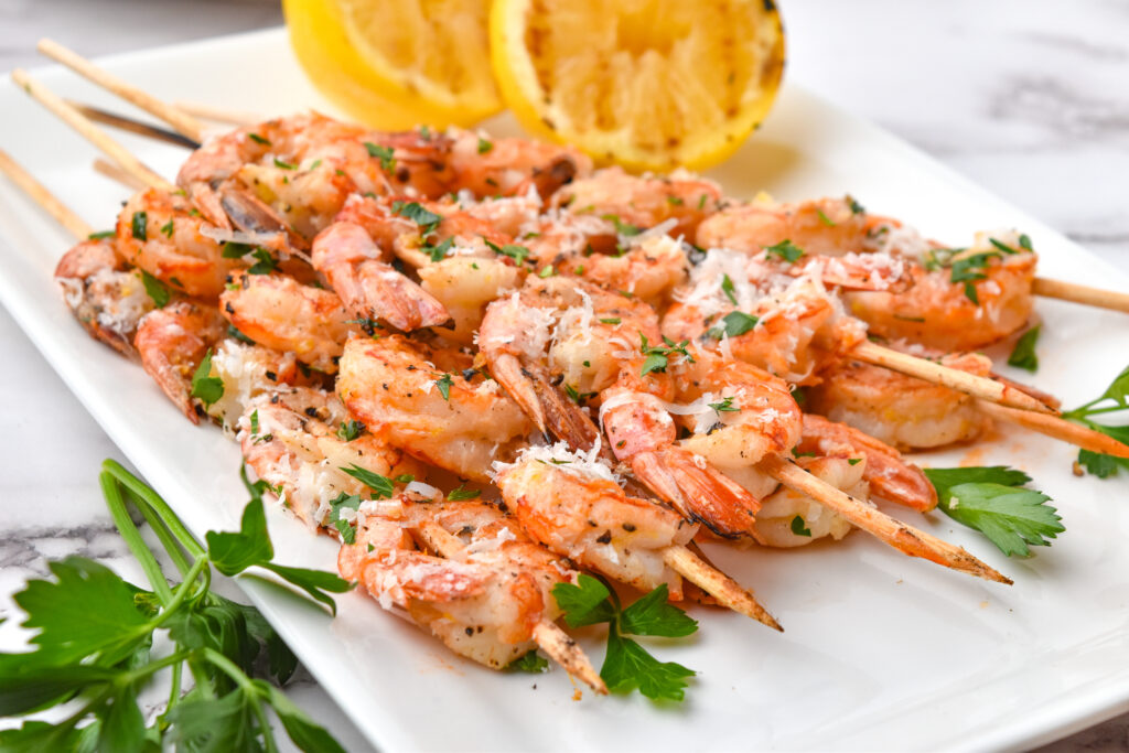 tray of grilled lemon garlic shrimp skewers with grilled lemon in back
