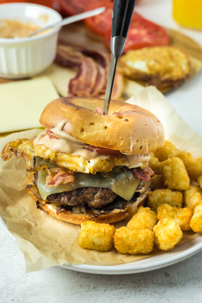 ultimate bagel burgers on plate with knife tucked into top bagel on a plate of tater tots