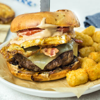breakfast bagel burger with tater tots on round plate with a serving knife on top