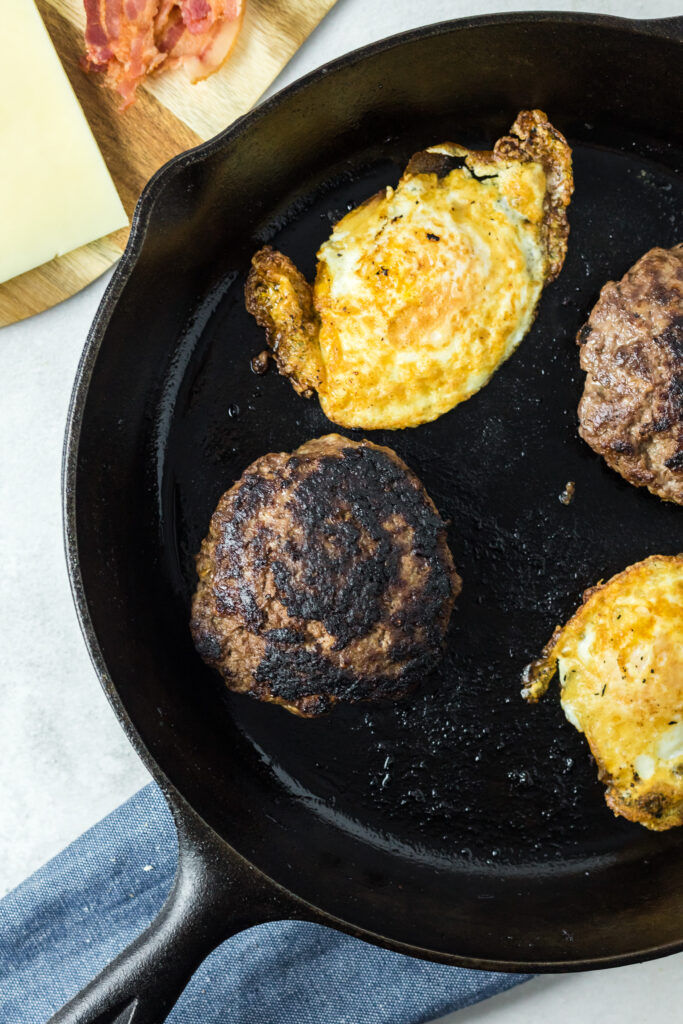 ultimate breakfast burgers with egg on top cooking in cast iron skillet
