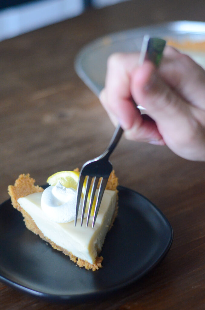 hand pushing fork through sour cream lemon pie on black plate