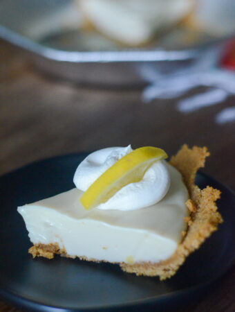 homemade creamy lemon pie on black saucer with colorful table runner and pan in back