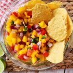 mango pico de gallo - mango chili salsa - in glass bowl with limes